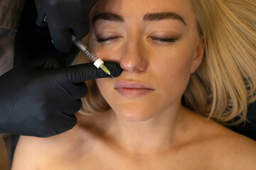 Doctor adds volume to woman's lips with lip filler, injection. White female lying on couch. Beauty...