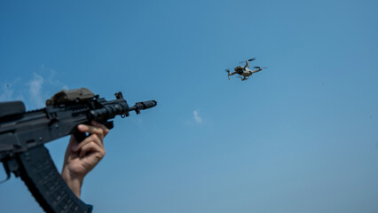 Fototapeta na wymiar A man aims to shoot a rifle at a flying drone against a blue sky. 