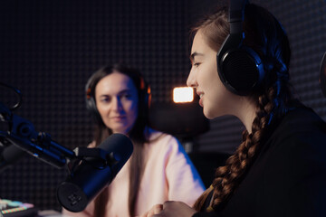 Female host and guest sitting at table with equipment while broadcasting radio program in recording...