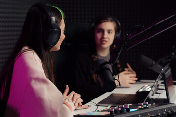 Female host and guest sitting at table with equipment while broadcasting radio program in recording...