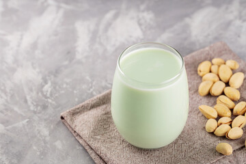 Homemade pistachio milk in a low glass on concrete. Organic pistachio milk and pistachios on a gray background. Copy space