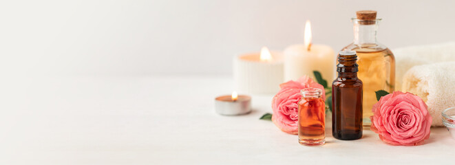 Obraz na płótnie Canvas Aromatherapy. Pure organic essential rose oil concept. Elixir with plant based floral herbal ingredients. Pink flowers extract. Spa atmosphere with candle, towel. White background. Banner copy space