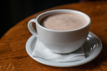 white cup with hot latte coffee on a wooden table. horizontal