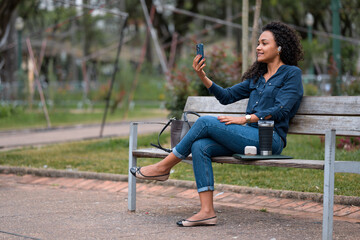 Young African American businesswoman smiling and looking at her smartphone while video chatting with friends in a public park