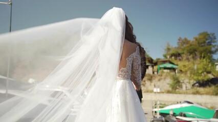 A white veil blowing in the wind. Couple standing near yacht. Slow motion