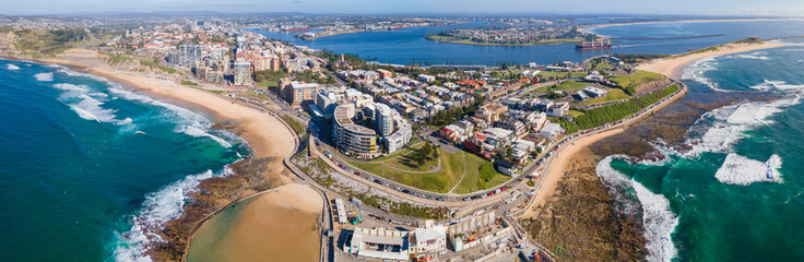 Panoramic aerial drone view of the harbour city of Newcastle, NSW, Australia as a cargo ship enters Newcastle Harbour on a sunny day  - obrazy, fototapety, plakaty