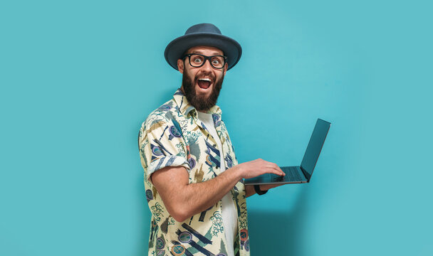 Young crazy bearded charismatic man. Shocked or surprised expression. Laptop concept. Funny promotion poster. Programmer, web developer holding a laptop in his hands and looking at the camera