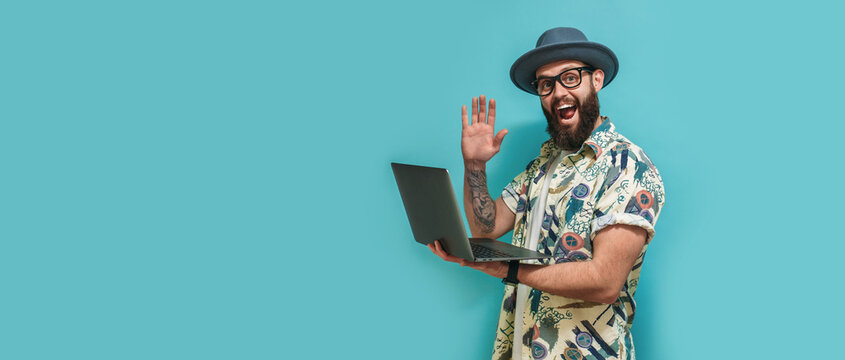 Young crazy bearded charismatic man. Shocked or surprised expression. Laptop concept. Funny promotion poster. Programmer, web developer holding a laptop in his hands and looking at the camera