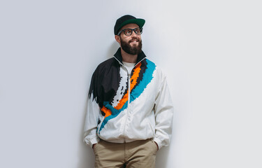Portrait of a stylish hipster model guy with a beard in glasses, a cap and a vintage tracksuit from the 90s-2000s.