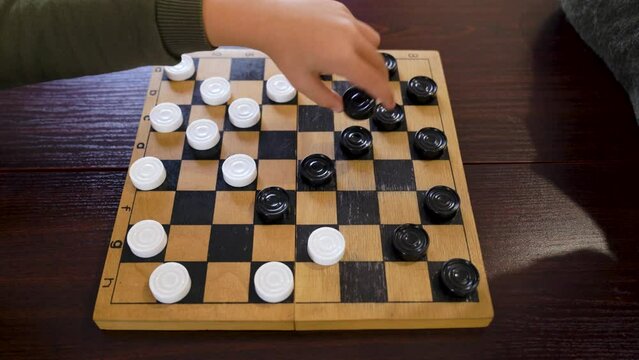 Grandmother and little grandson play checkers sit at table.