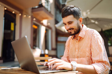 Young man  with laptop and phone sits in a cafe and works. Business, blogging, freelance, education concept.