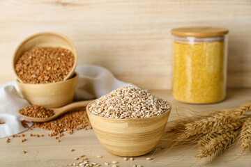 Bowl with pearl barley and spikelets on wooden background