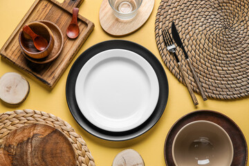 Beautiful table setting with plates, cutlery and wicker mats on yellow background