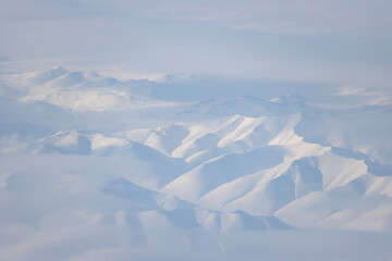 Fototapeta na wymiar Aerial view of snow-capped mountains and clouds. Winter snowy mountain landscape. Kolyma Mountains on the border of Kamchatka Territory and Magadan Region, Siberia, Far East Russia. Great background.