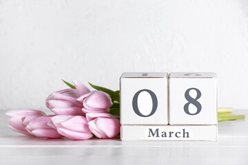 Cube calendar with date MARCH 8 and beautiful tulip flowers on table near white wall. Women's Day celebration