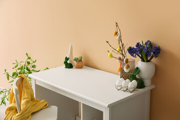 Workplace with tree branches, flowers in vases and Easter eggs near beige wall
