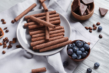 Plate with delicious chocolate wafer rolls and blueberries on grey wooden background