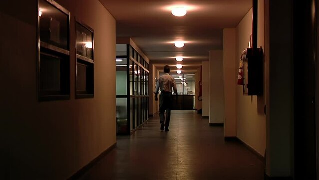 Man Walking along Corridor in an Argentine High School at Night.  