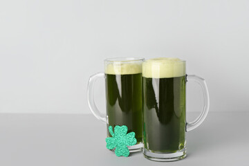 Glasses of beer and paper clover on grey background. St. Patrick's Day celebration