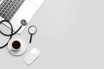Laptop with magnifier, stethoscope and cup of coffee on grey background. World Health Day