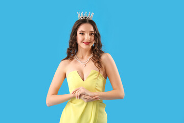 Beautiful young woman in prom dress and tiara on blue background