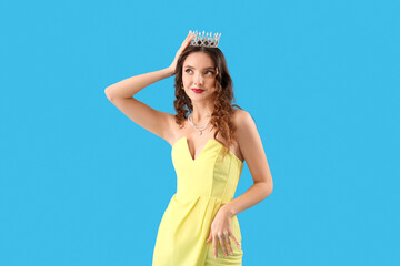 Beautiful young woman in prom dress and tiara on blue background
