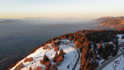 Winter view over a mountain covered with trees. Foggy sunset background.