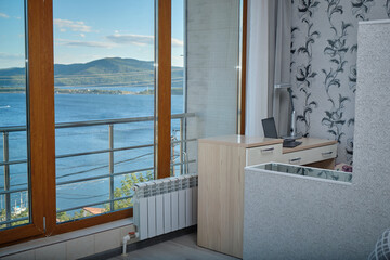An office with panoramic windows with a laptop on a table with a view of the sea during the daytime.