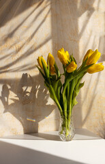 Yellow tulips in a vase in the evening rays of the sun. Holiday celebration concept. Interior decoration.