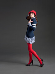 Vogue model in preppy outfit and red cloche hat striking a pose isolated on gray background - 575475284