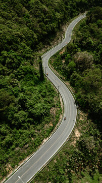 Top view of a country road in a green summer forest in the form of a winding curve with motorcycles. Rural landscape in Thailand. Aerial photography. © galaganov
