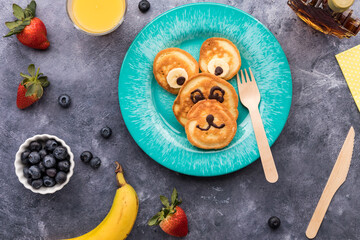 Bear shaped pancakes for a kid's breakfast, served with fruit and juice.