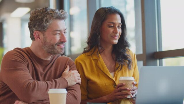 Mature male businessman brings takeaway coffee for female colleague as they have meeting with laptop together - shot in slow motion