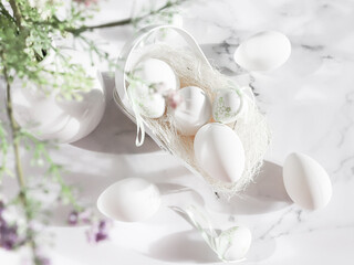 Decorative white eggs, a metal egg basket and a ceramic vase with spring flowers on a marble table