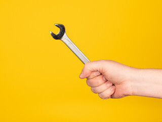A hand holds an open-end wrench. No face, yellow background.
