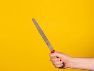 A hand holds a metal file. No face, yellow background.