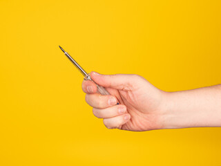 A hand holds a pen eletric tester. No face, yellow background.
