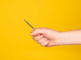 A hand holds a pen eletric tester. No face, yellow background.

