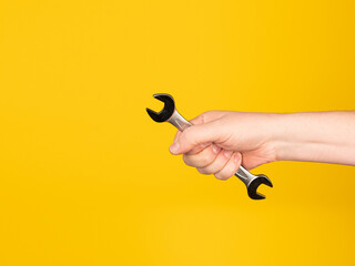 A hand holds an open-end wrench. No face, yellow background.
