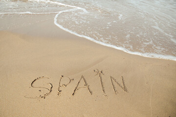 Spain lettering on the beach with wave and clear blue sea. 