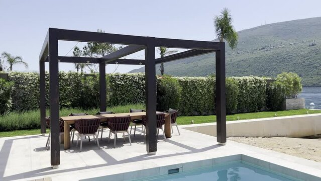 Table and chairs stand in a pergola by the pool on the seashore