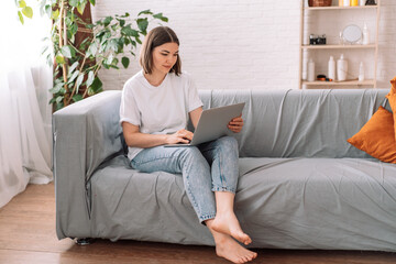 Obraz premium Lady freelancer sitting on gray sofa working with laptop.