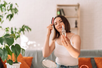 Lady holding glass bottle with pipette in front of her and combing her hair.