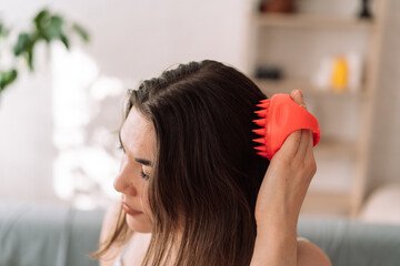 Girl enjoys doing herself a head massage using a scalp massager. - obrazy, fototapety, plakaty