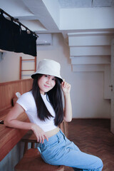 Beautiful Asian woman with a smile sits on a wooden table at a caf&eacute; near a lighting window. She smiled at the photographer as he took a snapshot of her with a pleased look.