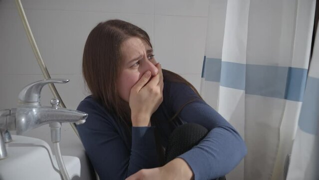 Afraid woman woman hiding in bathroom from criminal and closing her mouth with hand. Concept of domestic violence victim, stress, danger at home, fear.