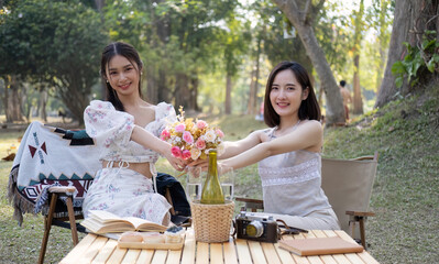 Gorgeous Asian woman giving a beautiful roses bouquet to her friend, having a special moment together in the park. female couple, lesbian, best friend, besties