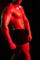 Man bodybuilder athlete with naked torso in sports uniform, isolated on black background in neon light. Advertising, sports, active lifestyle, colored light, competition, challenge concept. 