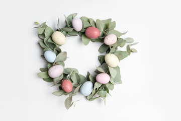 A beautiful Easter wreath made of eucalyptus leaves and pastel easter eggs, on a white background.
