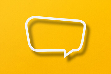 White paper cut out speech bubble shape set on yellow paper background.